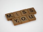 Close-up of Scrabble tiles arranged to spell 'Miss You' on a white background.