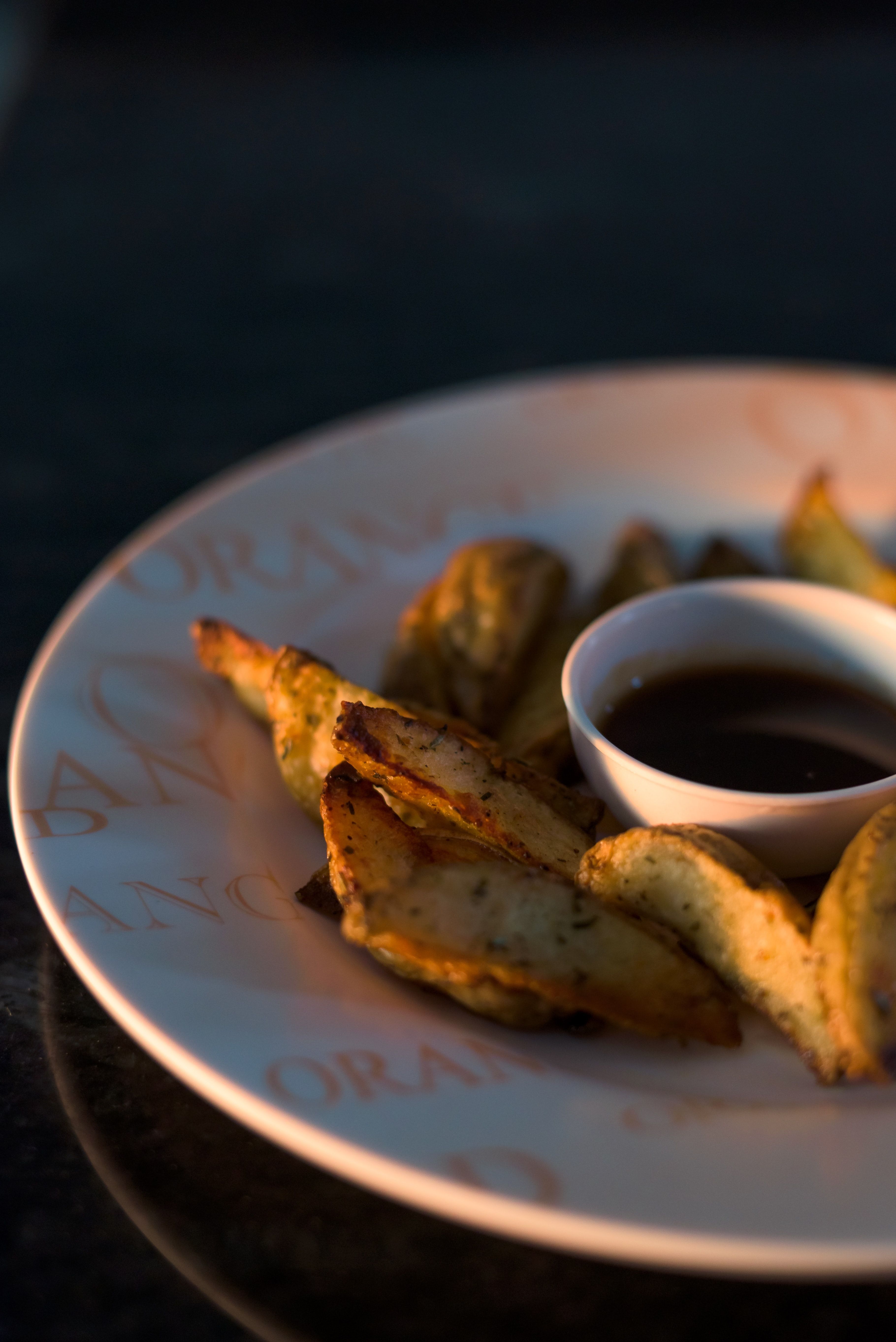 A sheet pan of golden, crispy roasted potato wedges with visible garlic bits and chopped rosemary, served on a dark plate.