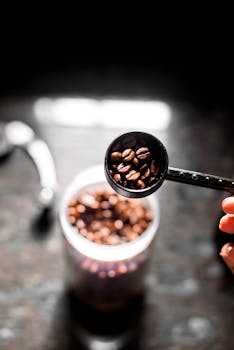Selective focus on roasted coffee beans in a scoop with blurred grinder background.