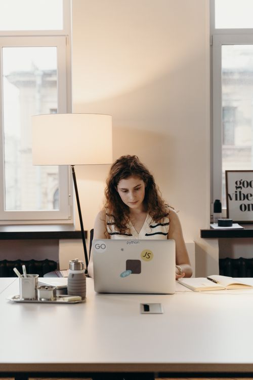 Free Focused young woman working on a laptop in a well-lit modern office interior. Stock Photo