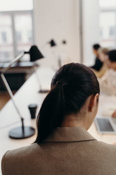 Back view of a professional woman working in a modern office setting with colleagues.