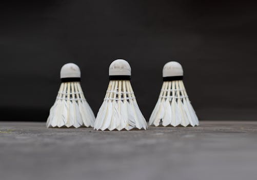 A detailed view of three white badminton shuttlecocks set against a dark background.