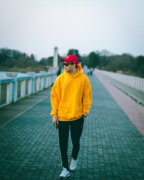 Man in a Yellow Hoodie Walking on a Bridge