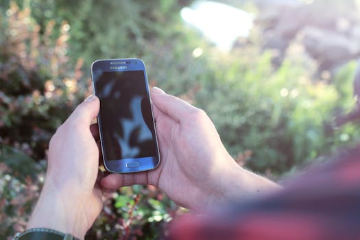Close-up of hands holding a smartphone outdoors with natural background.