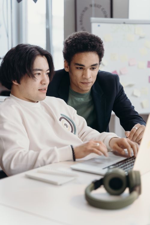 Free Two young professionals collaborating on a laptop in a modern office setting. Stock Photo