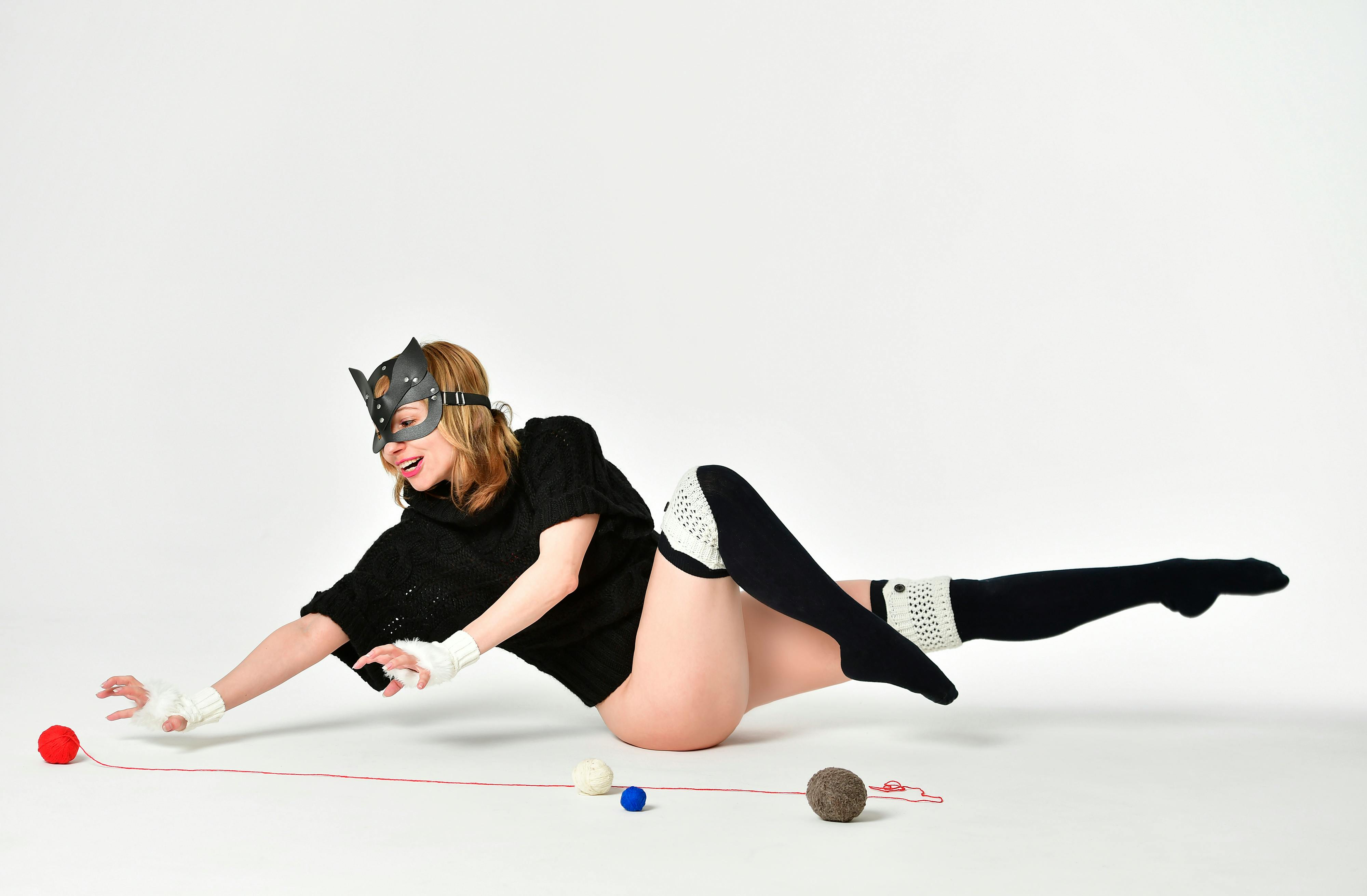 A woman in a cat-themed costume playing with colorful yarn balls in a studio setting.