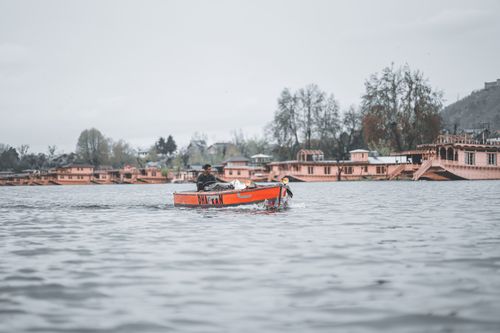 Free A man rows a vibrant boat on Dal Lake, passing scenic houseboats in the distance. Stock Photo