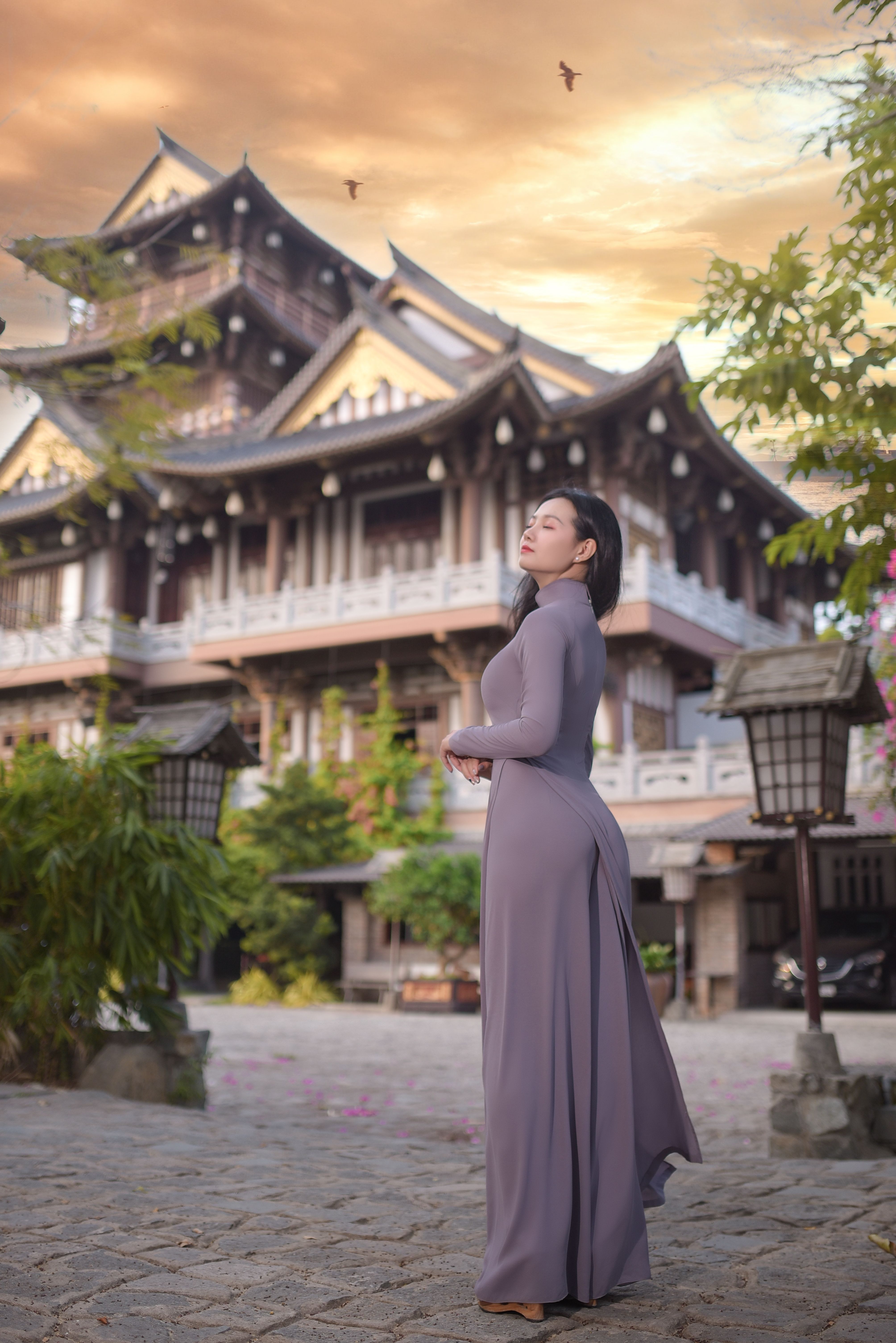 Woman in traditional dress standing in front of an Asian pagoda at sunset.