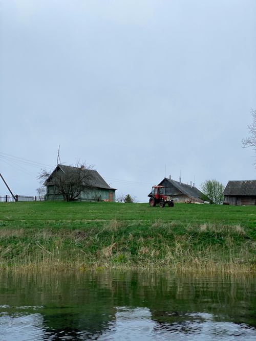 Free A serene rural landscape with barns, tractor, and reflecting river. Stock Photo