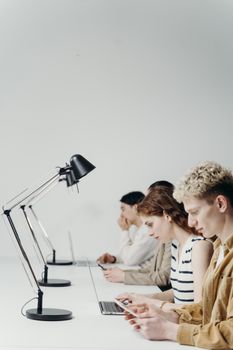 Group of young professionals using laptops at a modern office desk, emphasizing teamwork.