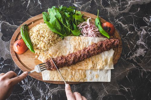 Free A mouthwatering Turkish kebab served with fresh vegetables and bulgur on a wooden plate. Stock Photo