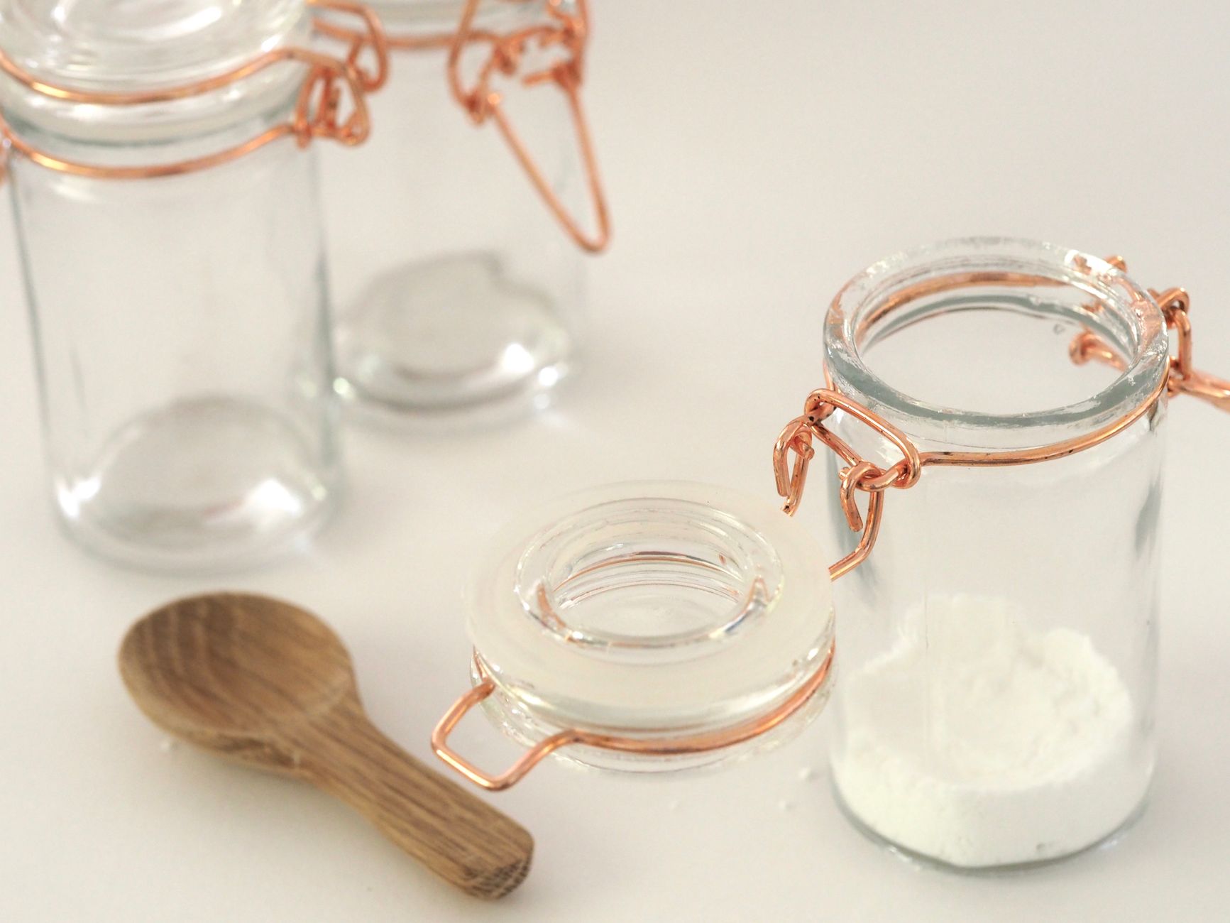 Close-up of glass jars with copper wire closures and a wooden spoon on a white background.