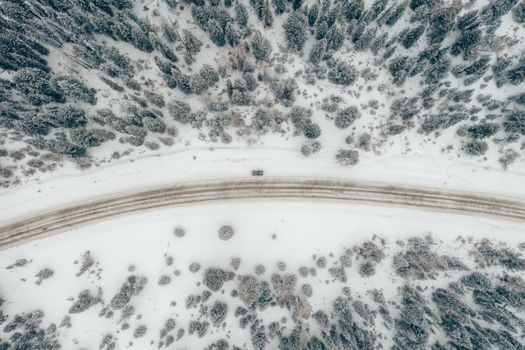 Drone shot of a snowy road through a forest in Russia, showcasing a lone vehicle and winter scenery.