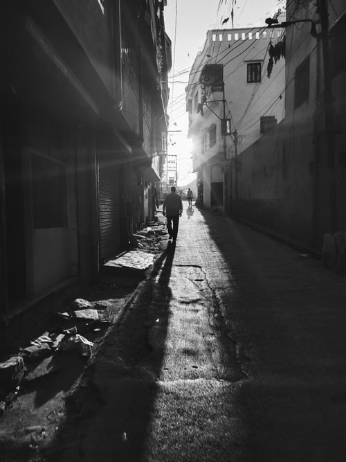 Free Black and white photo of a person walking down a shadow-filled alleyway at twilight. Stock Photo