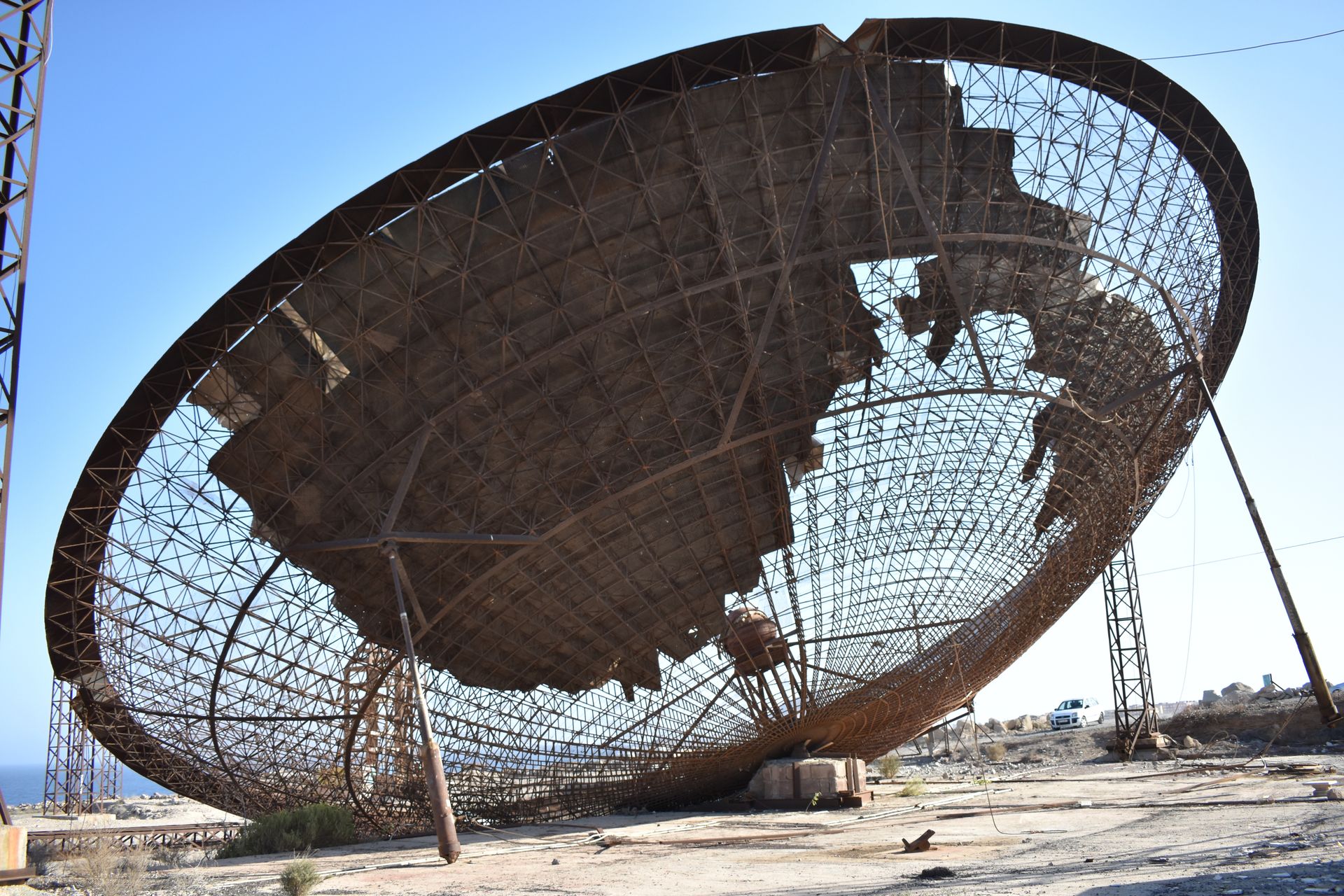 An old, rusted satellite dish in a barren desert landscape under a clear sky.