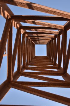 Looking up through a steel structure with sky backdrop, architectural abstraction.