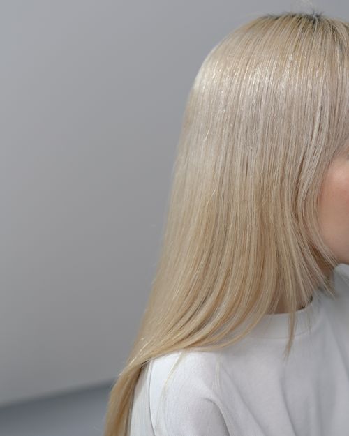 Free Detailed close-up of a woman's blonde hair with a neutral gray background, highlighting texture and color. Stock Photo