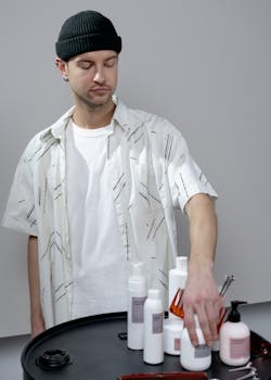 A barber arranging hair care products on a table, wearing a black hat and patterned shirt.