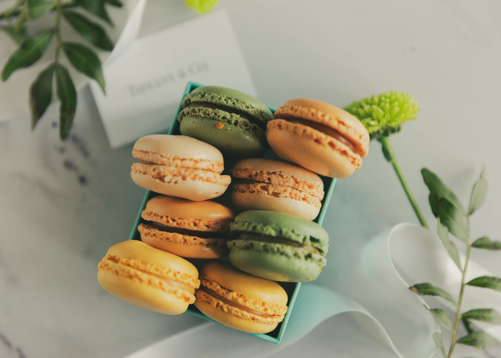 Elegant assortment of macarons in pastel colors in a Tiffany box with flower decor.