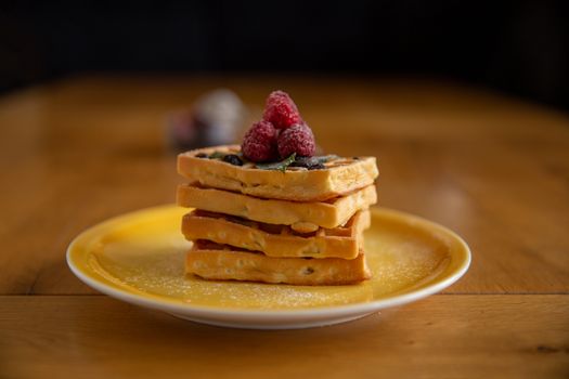 Close-up of golden waffles topped with fresh raspberries on a yellow plate, perfect for breakfast.