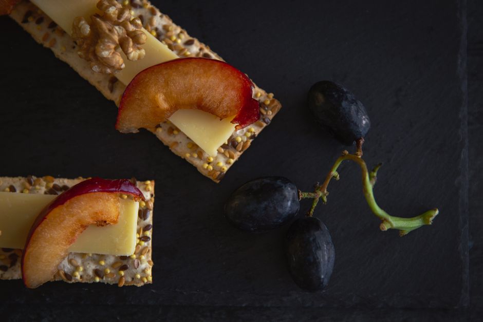 A close-up of a gourmet snack featuring cheese, walnuts, grapes, plums, and crackers.