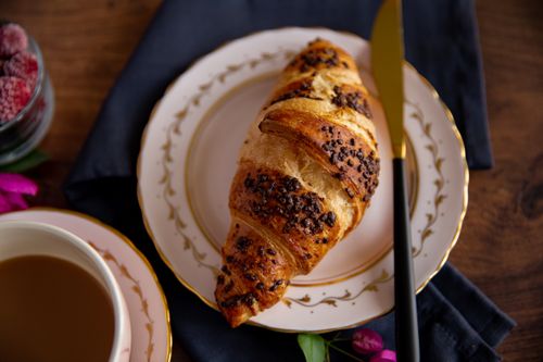 Free A beautifully laid breakfast featuring a chocolate croissant on a white plate with a cup of coffee. Stock Photo