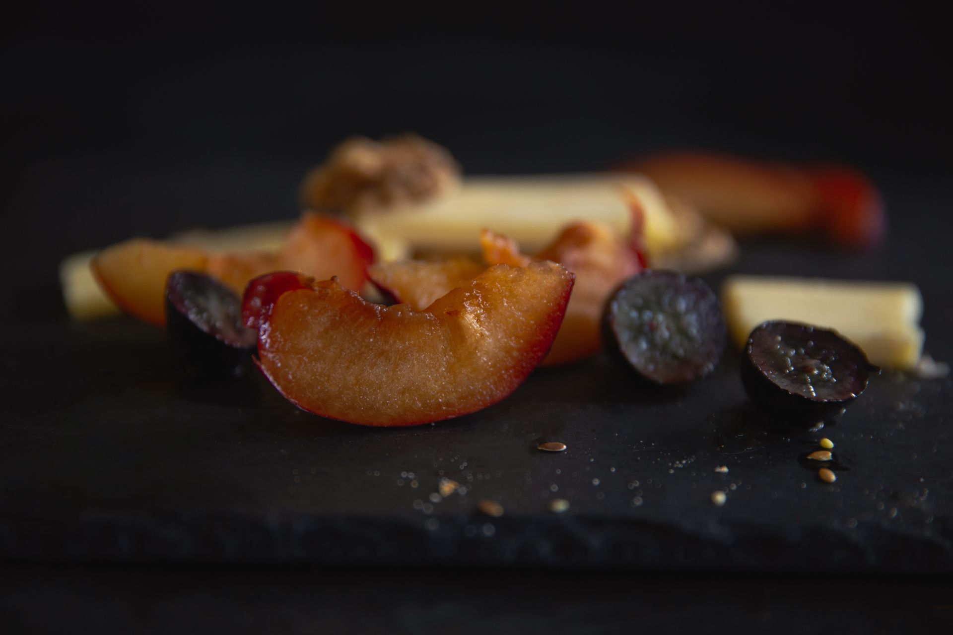Close-up of fresh plum slices on black slate with cheese and seeds. Perfect for food blogs and culinary visuals.