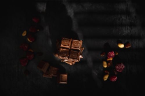 Free High-angle view of stacked chocolate bars with nuts and berries on a dark surface, featuring dramatic lighting. Stock Photo