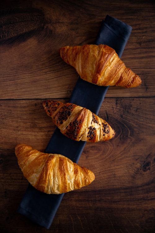 Free Top view of three golden croissants on a dark cloth over wooden table. Stock Photo