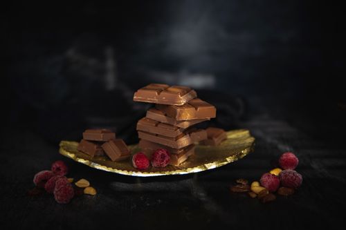 Free Indulge in a stack of chocolate bars with fresh raspberries on a golden plate. Stock Photo