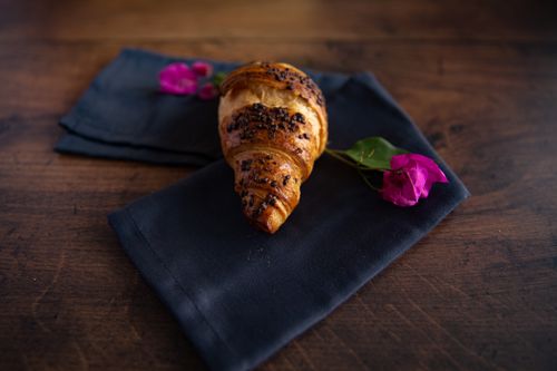 Free A freshly baked croissant on dark napkin with purple flowers, perfect for breakfast themes. Stock Photo