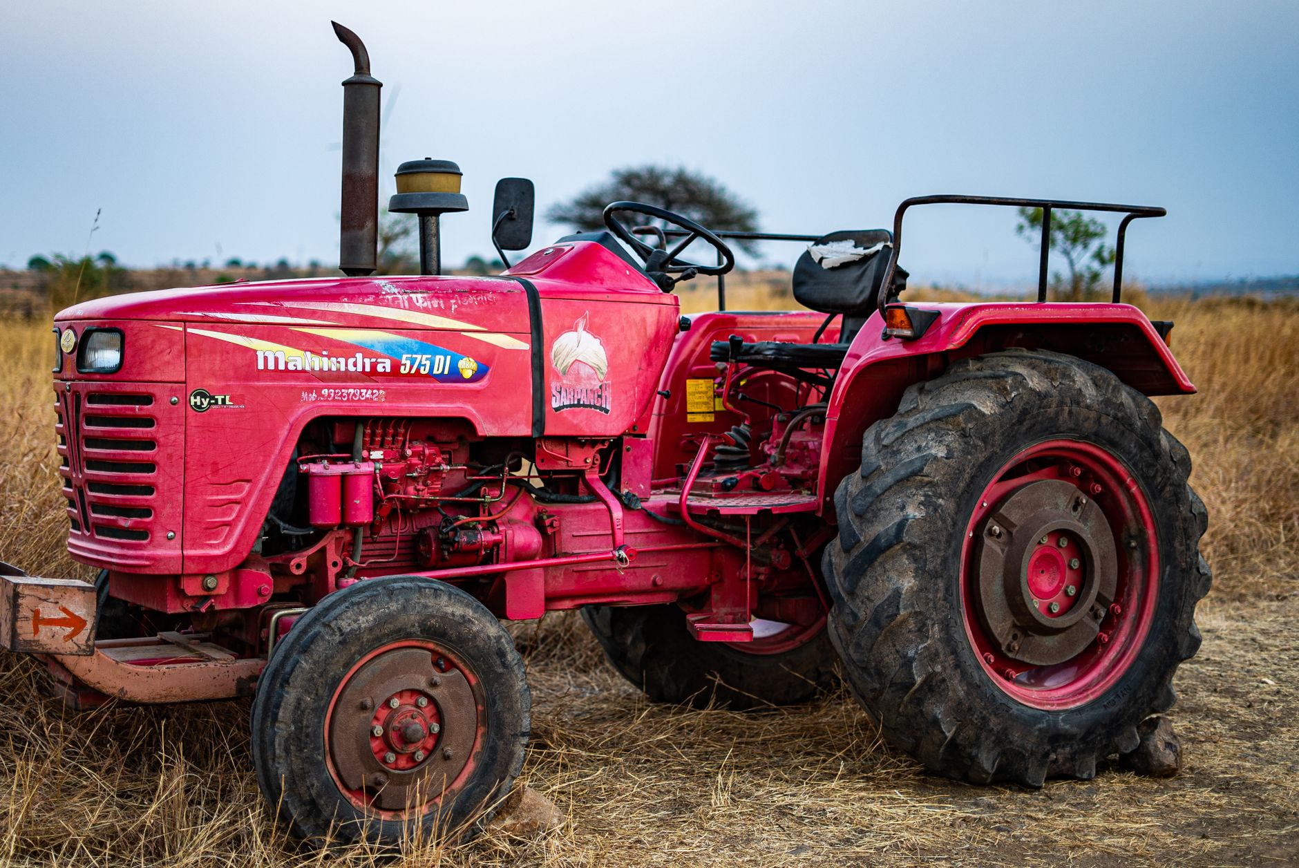 A vivid red tractor sitting idle in a dry, barren field under an overcast sky.