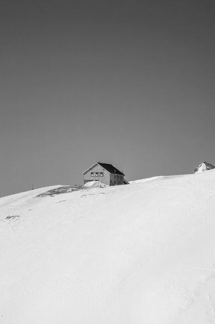 A remote wooden hut on a snow-covered slope in the Swiss Alps under a clear sky.