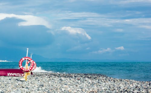 Red and White Ring Signage on Gravel Near Body of Water Under Blue and White Sky