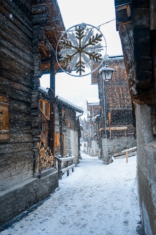 Free Snowflake Light Hanging Between Wooden Chalets While Snowing Stock Photo