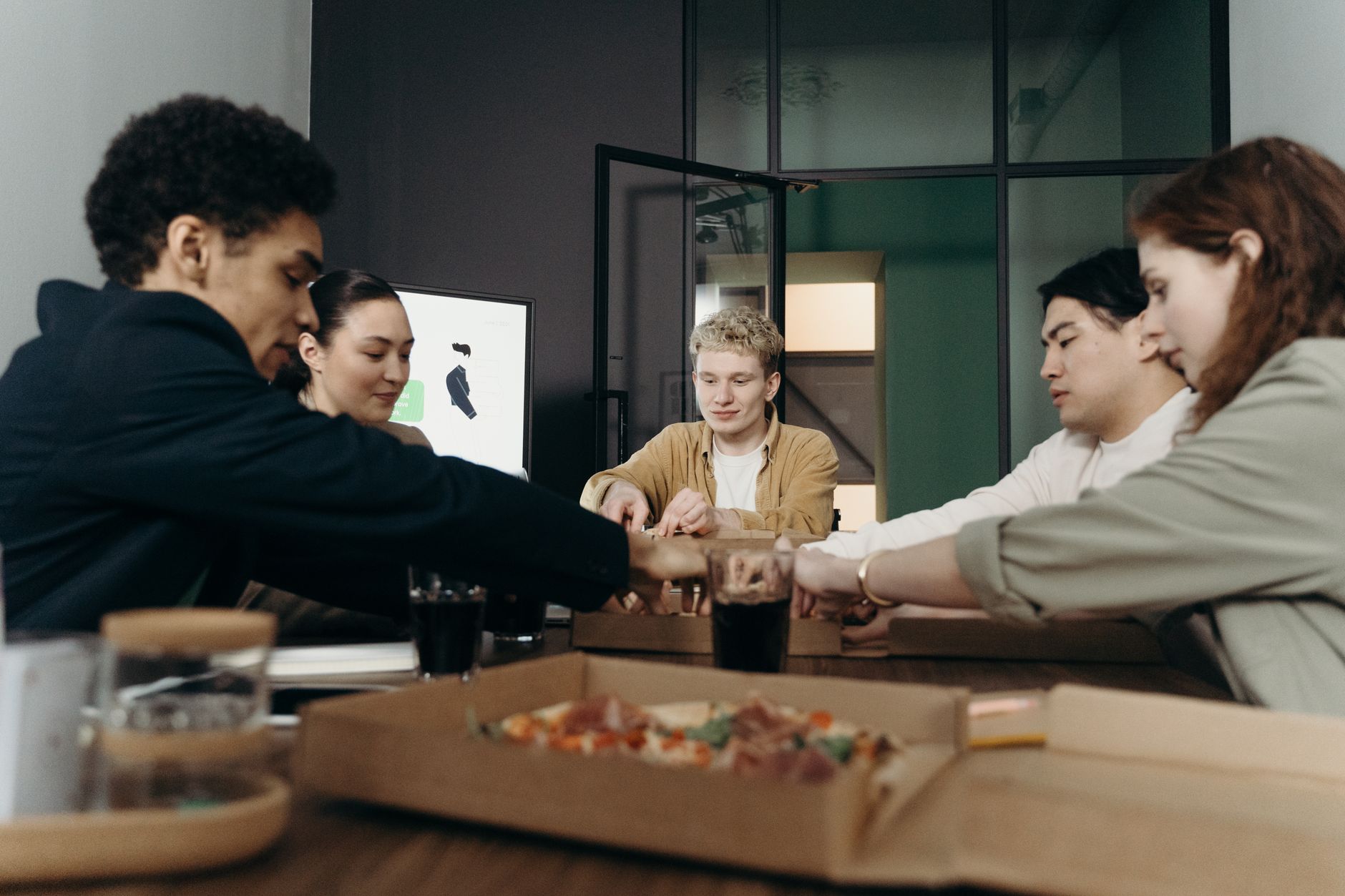 A diverse group of colleagues enjoying a pizza lunch break in a modern office setting.