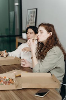 Diverse coworkers taking a break and enjoying pizza in an office setting, fostering teamwork and camaraderie.
