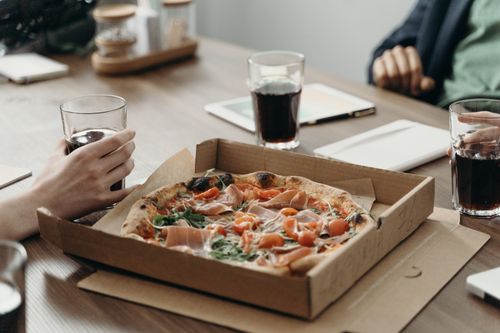 Free Office colleagues sharing a pizza and drinks during a casual lunch meeting. Stock Photo