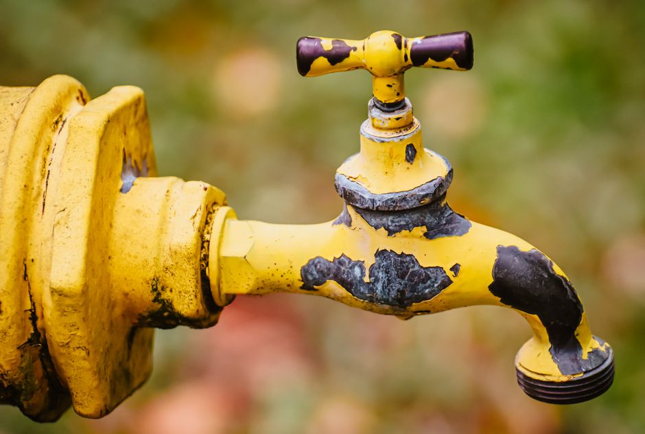 Detailed view of a worn yellow faucet with shallow focus and blurred background.