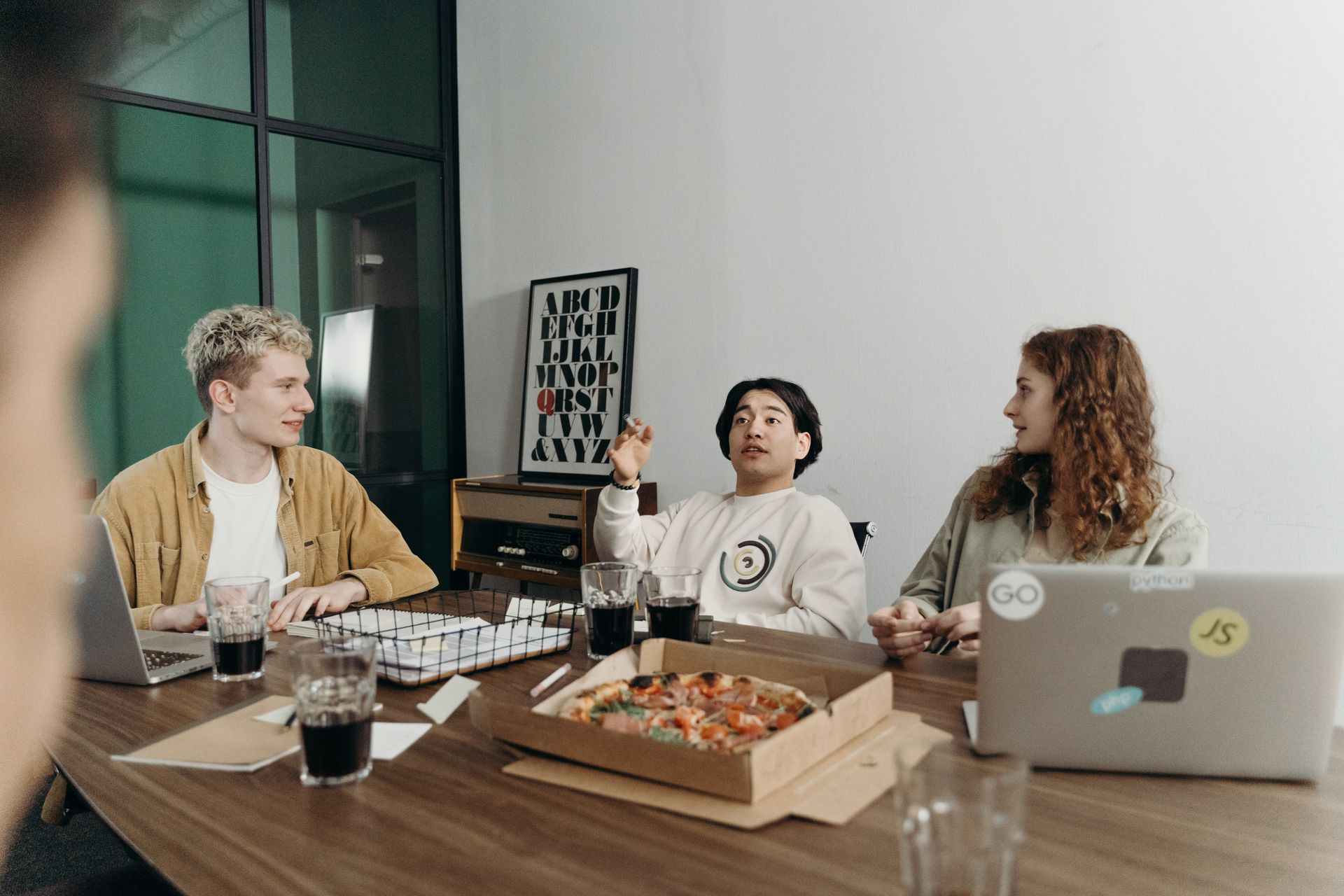 Young professionals brainstorm in a casual office setting with pizza and laptops.