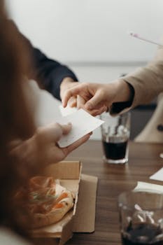 Hands exchanging ideas at a business lunch meeting with pizza and drinks.