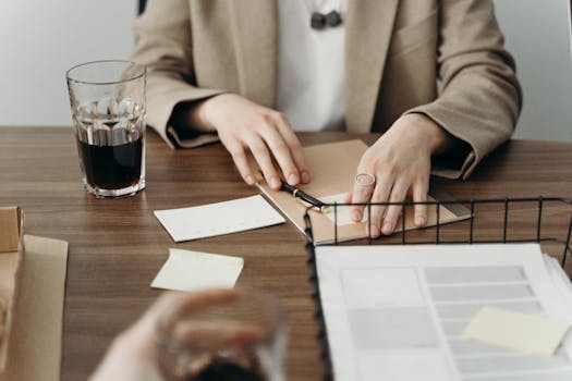 Hands organizing paperwork at a desk with a glass of dark beverage, portraying a business planning environment.