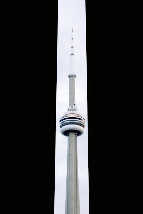 Free From below of modern tall CN Tower between silhouettes of multistory buildings against cloudy sky in Toronto Stock Photo