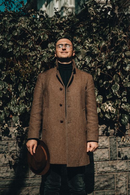 Free A fashionable man with a hat stands in sunlight in Istanbul, against an ivy-covered wall. Stock Photo