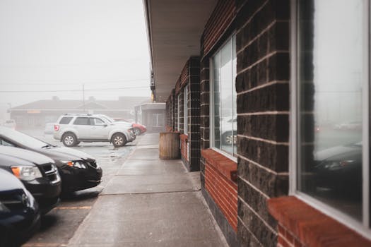 Cars parked on asphalt road near building on street in rainy weather in daylight