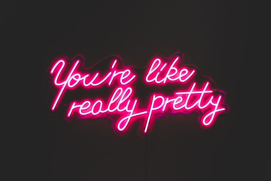 Bright pink neon inscription You are really pretty hanging on black wall in room