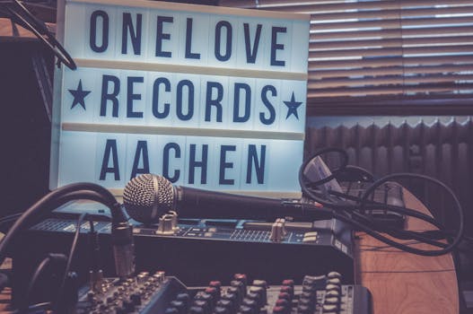A warm-toned studio featuring a microphone, audio mixer, and lightbox signage reading 'One Love Records Aachen'.