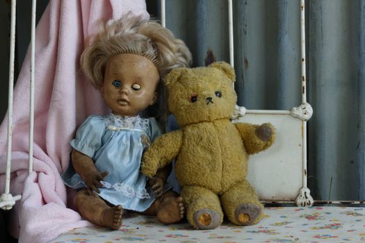 A vintage doll and teddy bear sit on a rusty bed frame, creating a nostalgic and eerie atmosphere.