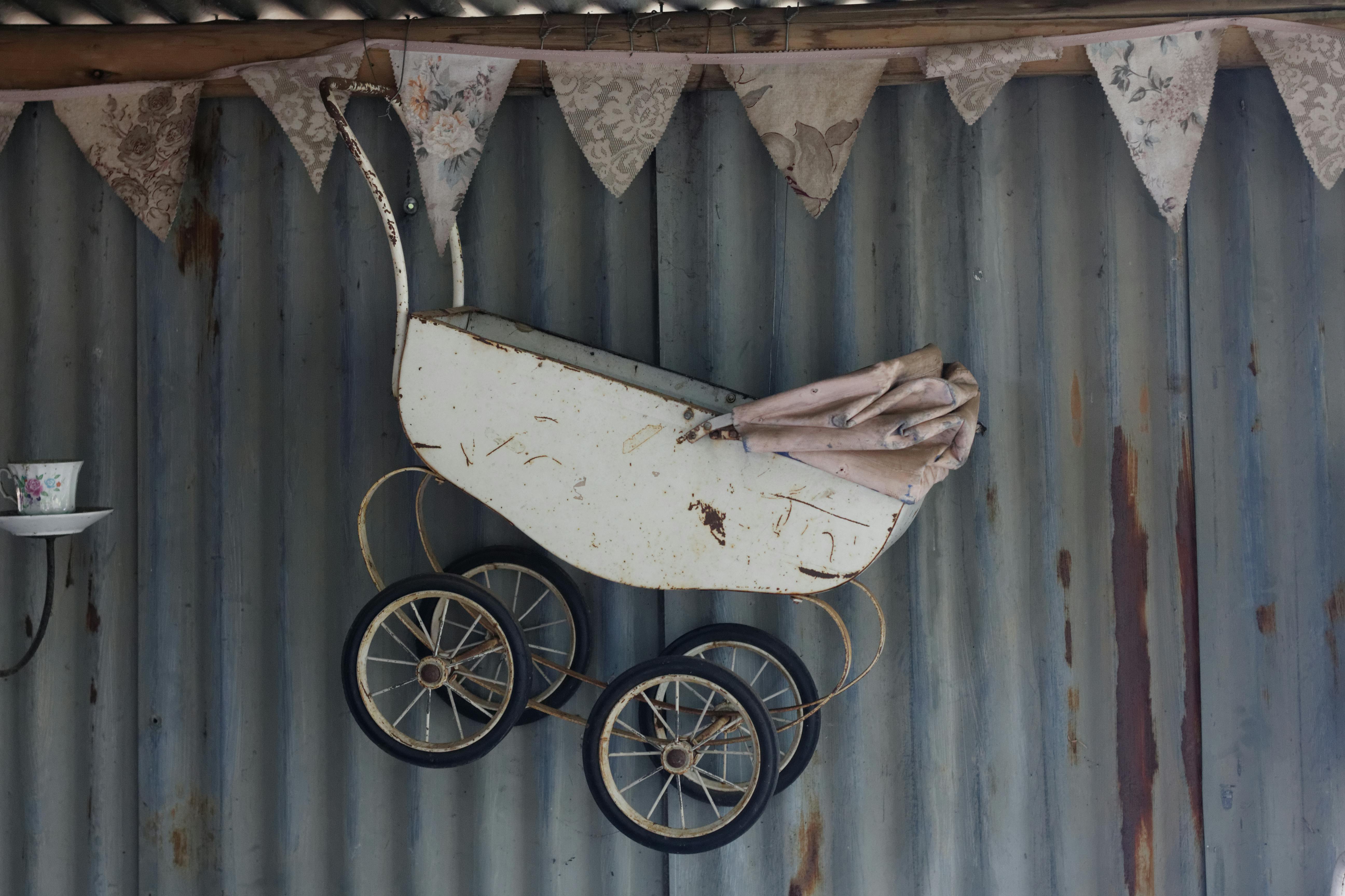 Old-fashioned baby carriage suspended on a rustic metal wall with bunting decor.
