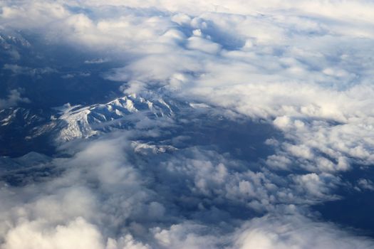 Stunning aerial photograph capturing snow-capped mountains blanketed in clouds, offering a serene natural vista.